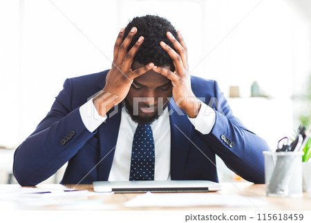 Stressed and overworked black young businessman sitting in office with hand on forehead, copy space Stressed and overworked black young businessman sitting in office with hand on forehead, copy space 115618459