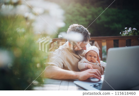Dad working from homeoffice, sitting on patio with laptop, holding little baby girl. Father spending time with small daughter, enjoying together time. Father's Day. 115618460