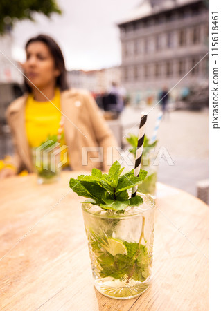 Young woman at a city cafe, sipping a Mojito with modern buildings, creating a trendy atmosphere 115618461