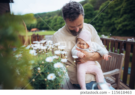 Father holding cute baby in arms, sitting on wooden patio and enjoying beautiful weater with his baby daughter. Father's Day 115618463