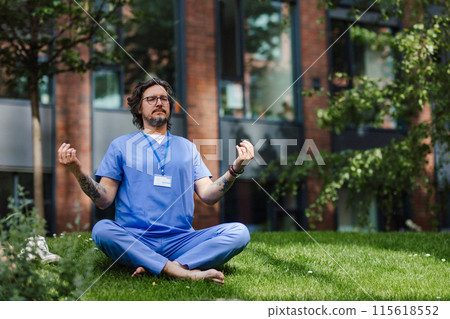 Doctor sitting on grass, meditating and relaxing, winding down from busy workday in hospital. Mental health and life balance for a healthcare worker. 115618552