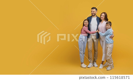A happy family, consisting of a mother, father, daughter, and son, stand closely together while embracing each other. They are all smiling and looking directly at copy space 115618571