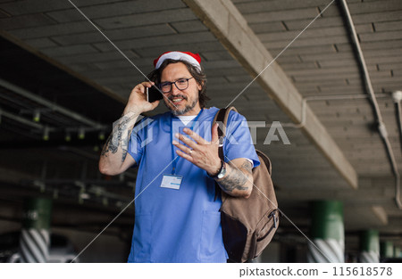 Portrait of male nurse with christmas hat making call. Working in hospital on Christmas day, Christmas Eve. Doctor working a Christmas shift and can't be with family. Portrait of male nurse with christmas hat making call. Working in hospital on Christmas day, Christmas Eve. Doctor working a Christmas shift and can't be with family. 115618578