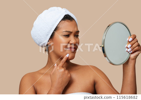 A woman is standing in front of a mirror, closely examining her own face. She appears focused and engaged, likely inspecting her skin or features. The mirror reflects her image back at her. 115618682