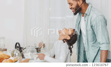 Help me, daddy. Cute black girl asking father to help her with cookies making, mixing dough ingredients, kitchen interior, copy space 115618767