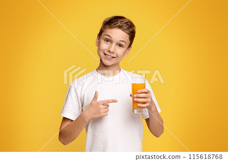 A young boy standing and holding a glass filled with orange juice. 115618768
