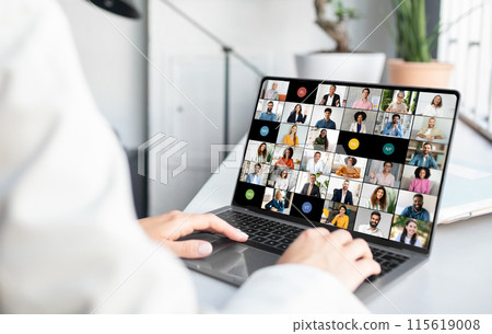 Woman sitting at a desk, actively engaged with a laptop screen displaying a group of people in a video call. The individual appears focused on the virtual meeting Woman sitting at a desk, actively engaged with a laptop screen displaying a group of people in a video call. The individual appears focused on the virtual meeting 115619008