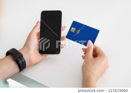 Hands of young european woman use smartphone with blank screen and credit card on white table in office, cropped. Banking, business and work, device and shopping, sale app, order and pay 115619060