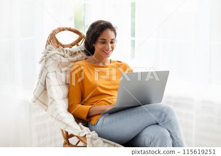Freelance. Happy Middle Eastern Young Woman Using Computer Working Online On Laptop, Sitting In Comfortable Chair At Cozy Home Interior. Internet Technology, Distance Work And Study 115619251