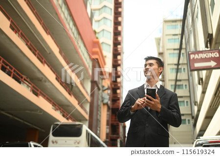 Successful businessman holding smartphone looking away while walking on city street Successful businessman holding smartphone looking away while walking on city street 115619324