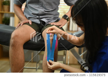 Physical therapist male athlete applying kinesio tape on knee for safety muscle and joint. Rehabilitation concept Physical therapist male athlete applying kinesio tape on knee for safety muscle and joint. Rehabilitation concept 115619373