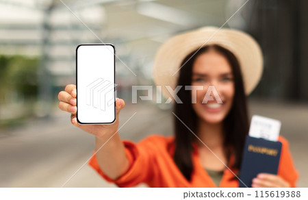 Travel Smart with Mobile Technology. Happy Lady Showing Blank Phone Screen Holding Boarding Pass in Passport, Promoting Travel App for Online Ticket Booking Outdoor. Mockup, Selective Focus 115619388