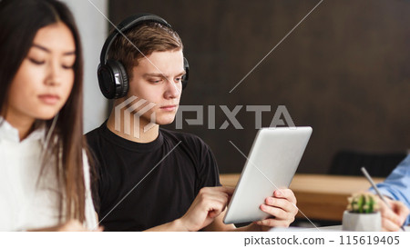 College student surfing internet on tablet in library, listening music in headphones, free space College student surfing internet on tablet in library, listening music in headphones, free space 115619405