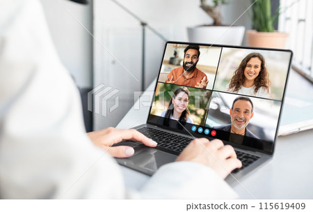 Lady sitting at a laptop is engaged in a video conference with a group of people displayed on the screen. The individual appears focused as they interact digitally with their remote team. 115619409