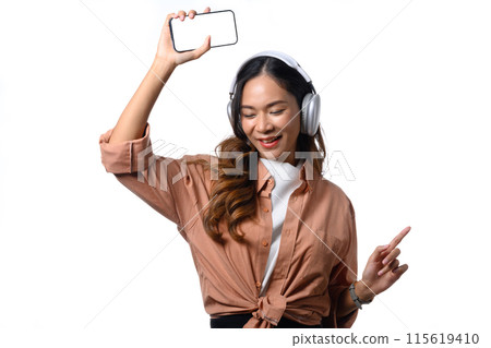 Cheerful young woman listening music with headphones and dancing on white background 115619410