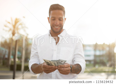 First salary. Happy young businessman holding fan of money, celebrating big financial luck and success, standing outdoors. Profit and wealth concept 115619432