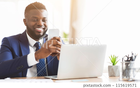 Happy african american businessman chatting on smartphone, sitting in modern office, copy space 115619571