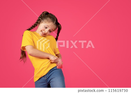 Cheerful preteen girl putting credit card into her pocket while standing isolated over pink studio background, happy cute little female child enjoying money saving and bank services, copy space 115619730