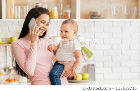 A woman holding a baby in her arms while engaging in a phone conversation. She appears focused on the call while balancing the child. Multi-tasking as a caregiver and communicator. A woman holding a baby in her arms while engaging in a phone conversation. She appears focused on the call while balancing the child. Multi-tasking as a caregiver and communicator. 115619736