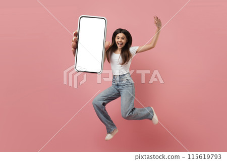Joyful teen girl jumping in air with big blank smartphone in hand, carefree female teenager demonstrating empty mobile phone, young woman having fun on pink studio background, collage, mockup 115619793