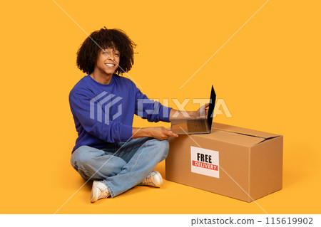 A guy is seated on the floor, with a cardboard box beside him and a laptop open in front, appears focused on the screen, possibly working or studying. 115619902
