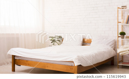 A bed is positioned next to a window in a bedroom. The room is illuminated by natural light filtering through the window. The bed is made with clean linens and pillows A bed is positioned next to a window in a bedroom. The room is illuminated by natural light filtering through the window. The bed is made with clean linens and pillows 115619943