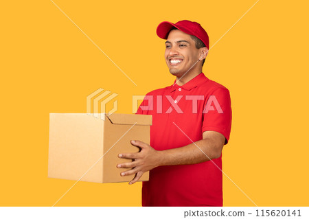 A cheerful delivery man in a red uniform and cap holds a cardboard package while smiling, set against a vibrant yellow background. 115620141