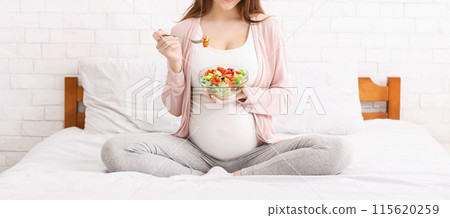 Pregnancy and healthy organic nutrition. Unrecognizable pregnant woman eating natural vegetable salad in bed, panorama 115620259