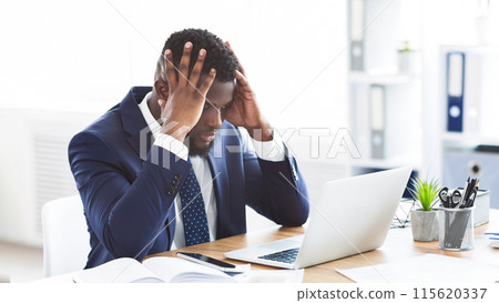 Stressed and overworked african-american young businessman sitting in office with hand on forehead, copy space 115620337