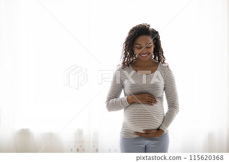 Portrait Of Beautiful Black Pregnant Woman Standing Near Window At Home, Embracing Belly. Young African American Expectant Mother Tenderly Touching Tummy And Smiling, Enjoying Pregnancy, Copy Space Portrait Of Beautiful Black Pregnant Woman Standing Near Window At Home, Embracing Belly. Young African American Expectant Mother Tenderly Touching Tummy And Smiling, Enjoying Pregnancy, Copy Space 115620368