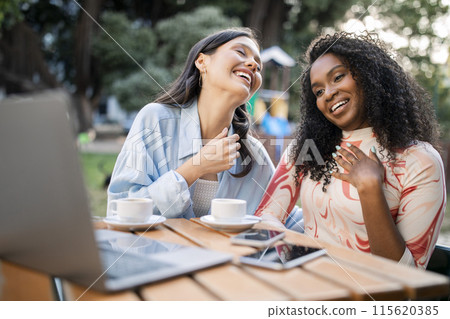 Two Happy Laughing Young Women Using Laptop In Cafe Outdoors, Cheerful Positive Multietnic Female Friends Watching Videos On Computer And Drinking Coffee, Enjoying Time Together, Closeup Two Happy Laughing Young Women Using Laptop In Cafe Outdoors, Cheerful Positive Multietnic Female Friends Watching Videos On Computer And Drinking Coffee, Enjoying Time Together, Closeup 115620385