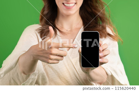 Happy young european lady point finger at smartphone with blank screen, isolated on green studio background, close up. Recommendation sale, website and app for shopping, ad and offer Happy young european lady point finger at smartphone with blank screen, isolated on green studio background, close up. Recommendation sale, website and app for shopping, ad and offer 115620440