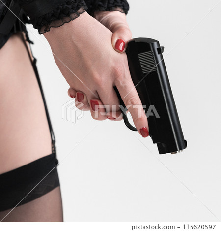 Close-up view of woman's hands with gun and part of her legs in stockings with garters. Cropped side view of an unrecognizable real woman body part in lingerie with pistol on white background 115620597