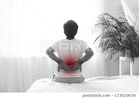 Black and white photo of unrecognizable man in pajamas touching lower back while sitting on bed at home, young male suffering from acute backache in the morning, uncomfortable sleeping concept Black and white photo of unrecognizable man in pajamas touching lower back while sitting on bed at home, young male suffering from acute backache in the morning, uncomfortable sleeping concept 115620630