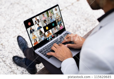African American man sits on a bench with his laptop, engaging in an early morning virtual meeting. Several participants are visible on the screen in a video conference format. African American man sits on a bench with his laptop, engaging in an early morning virtual meeting. Several participants are visible on the screen in a video conference format. 115620685