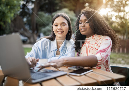 Happy Multiethnic Female Friends Using Laptop Computer Together Outdoors At Cafe Terrace, Two Smiling Young Women Typing On Keyboard, Browsing Internet Or Shopping Online While Relaxing Outside Happy Multiethnic Female Friends Using Laptop Computer Together Outdoors At Cafe Terrace, Two Smiling Young Women Typing On Keyboard, Browsing Internet Or Shopping Online While Relaxing Outside 115620717