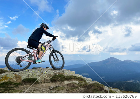 Cyclist man riding electric mountain bike outdoors. Male tourist biking along grassy trail in the mountains, wearing helmet. Concept of sport, active leisure and nature. 115620769