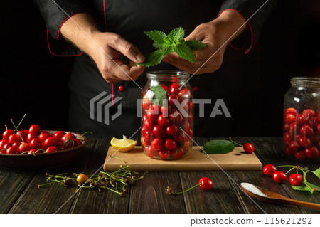 Adding aromatic green mint to a jar of cherries by hand before canning. Concept for making a delicious sweet cherry compote Adding aromatic green mint to a jar of cherries by hand before canning. Concept for making a delicious sweet cherry compote 115621292