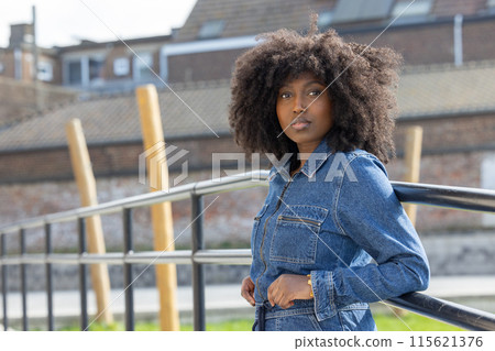 A young woman is striking a pose outdoors, wearing a denim jacket with an urban background A young woman is striking a pose outdoors, wearing a denim jacket with an urban background 115621376