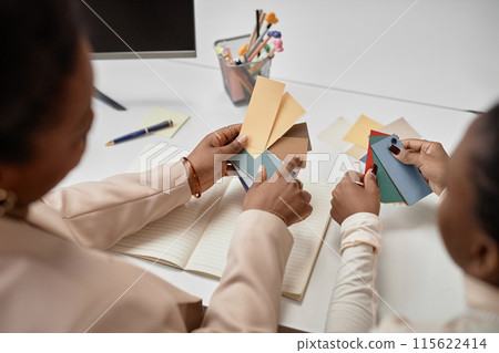 Close up shot of female hands holding paper swatches in pastel colors against working desk with pens and notebook, creativity work concept 115622414