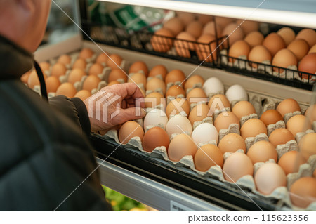 Close-up of an elderly person's hand picking eggs from a supermarket shelf 115623356