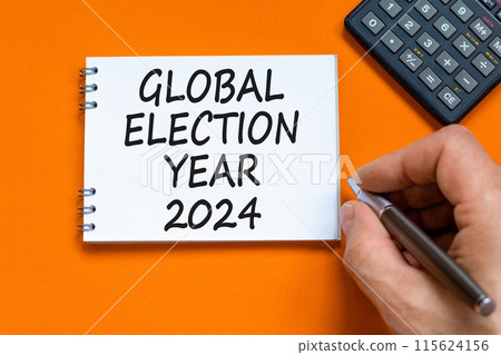 Global election year 2024 symbol. Concept words Global election year 2024 on beautiful white note. Beautiful orange background. Voter hand. Business Global election year 2024 concept. Copy space 115624156