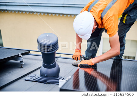 Worker building photovoltaic solar panel system on rooftop of house. Man engineer in helmets and gloves installing solar module with help of hex key outdoors. Renewable energy generation concept. Worker building photovoltaic solar panel system on rooftop of house. Man engineer in helmets and gloves installing solar module with help of hex key outdoors. Renewable energy generation concept. 115624500