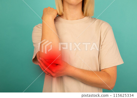 young woman experiencing pain in elbow joint on blue background. 115625334