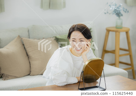 Middle-aged woman looking in the mirror in the living room 115625440