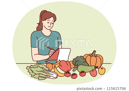 Woman nutritionist is standing near table with vegetables and making notes in notebook 115625706