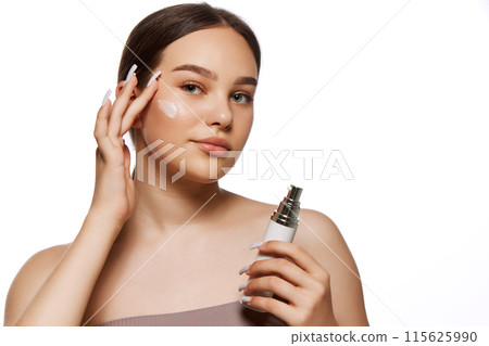 young face protection. Portrait of young girl taking care after her well-kept skin, applying cream isolated on white background 115625990