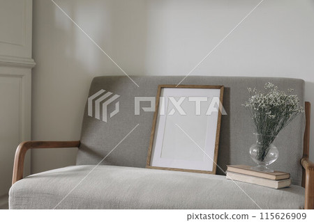 Minimal Scandinavian interior. Blank wooden picture frame mockup. Glass vase with dry limonium flowers, old books. Elegant midcentury linen sofa. White wall background. Home office concept. 115626909