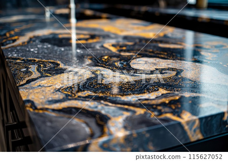 Close-up shot of a glossy epoxy resin art piece with swirling black and gold patterns 115627052
