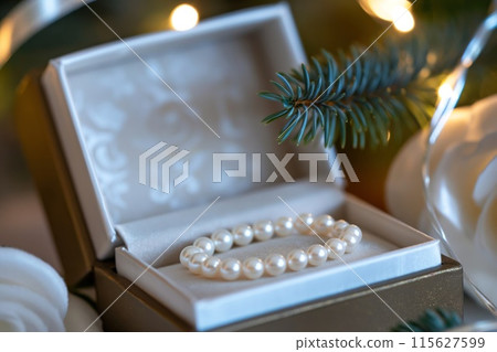 Close-up of a pearl bracelet in an open gift box, adorned with Christmas tree branches 115627599